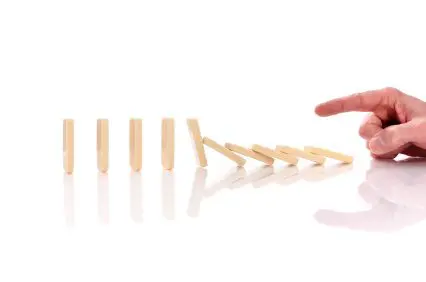 Finger pushing a domino that is knowing over several more dominos. Set against a pure white background.