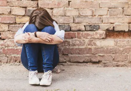 Scared millennial girl sitting alone in the city next to a brick wall