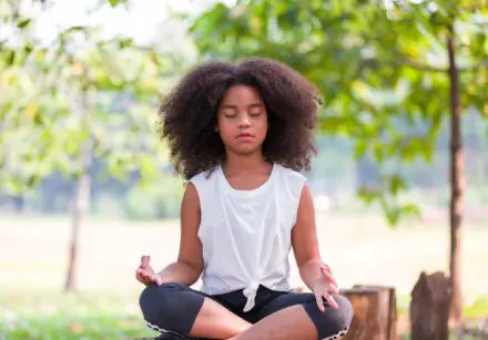 African American little girl doing meditate yoga asana with eyes closed outdoor in park. Kids girl practicing doing yoga outdoor