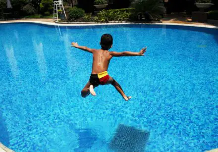 Boy leaps into swimming pool with arms outstretched