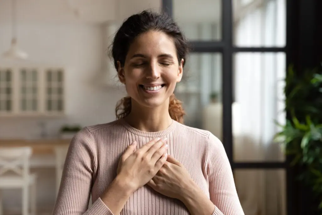 Dark haired woman with eyes closed, smiling, with her hands on her heart.