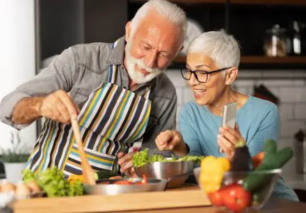Vibrant ageing couple cooking a health meal together, smiling.