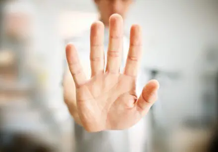 Man showing stop gesture with his hand out front. His face and body are blurred in the background and only the hand out in front is in focus.