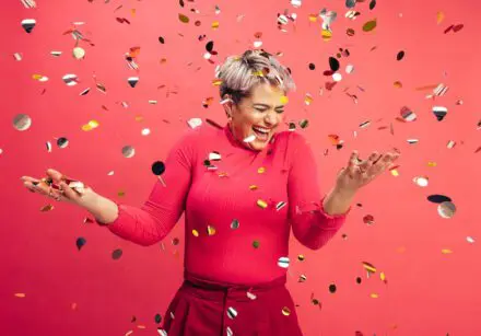 Woman celebrating. Red background. Pieces of silver paper floating.