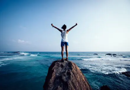 Young woman outstretched arms on seaside rock cliff edge