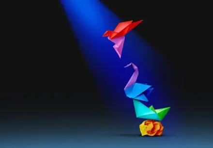 Transformation of a piece of crumpled yellow paper into a succession of coloured paper-folded animals, and finally into a brightly pink and red coloured paper-folded bird, which is now taking flight. The background is black and a light is shining on the bird.