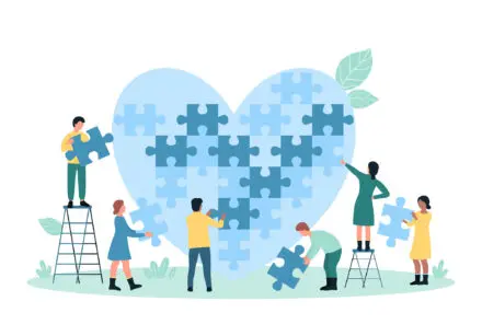cartoon of 6 people (3 males, 3 females) building a giant pale blue heart out of giant jigsaw pieces.