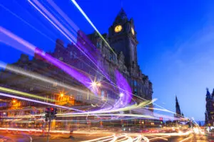 Edinburgh at night scene with Lights streak from high-sided vehicles on Princess street and Balmoral hotel on background. The sky is dark blue.