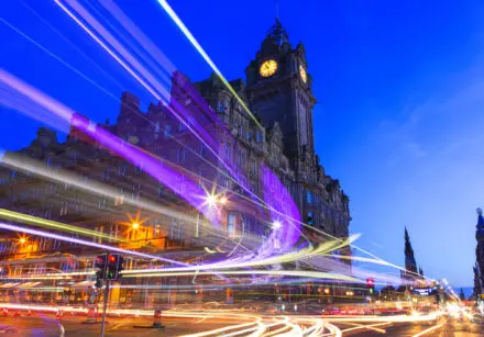 Edinburgh at night scene with Lights streak from high-sided vehicles on Princess street and Balmoral hotel on background. The sky is dark blue.