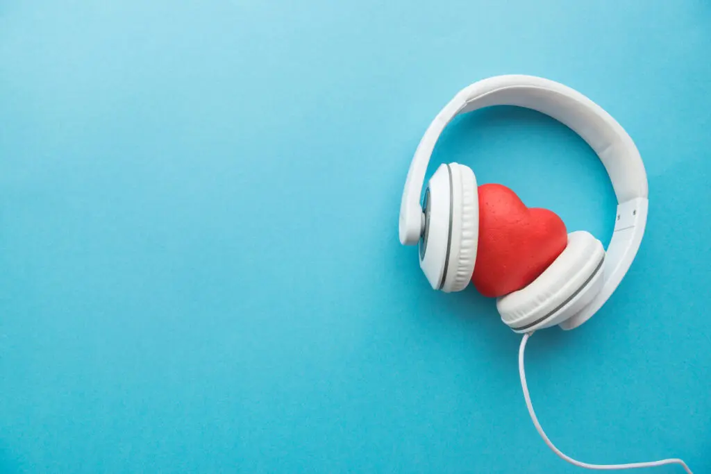 Image of a red heart wearing white bulky earphones. It's on an aqua-coloured background.