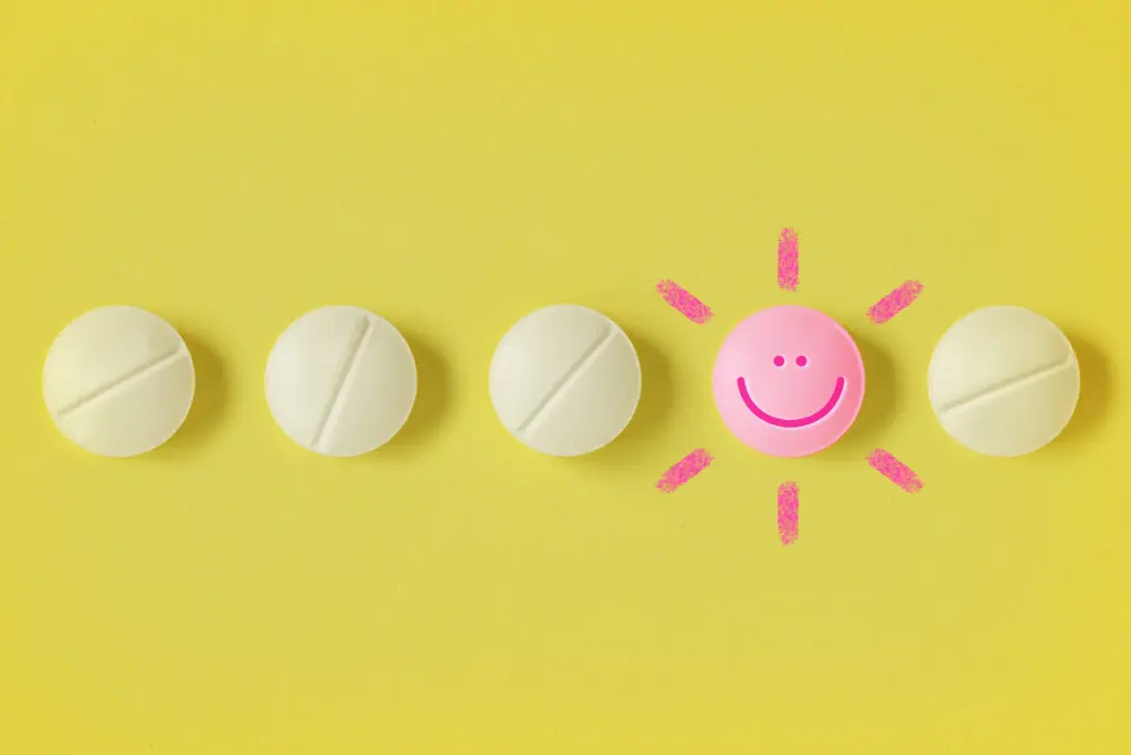 Row of five tablets in a horizontal row on a bright yellow background. Four of the tablets are pale yellow. The second from the right is bright pink, has a smiley face, and sunshine emanations coming out of it.