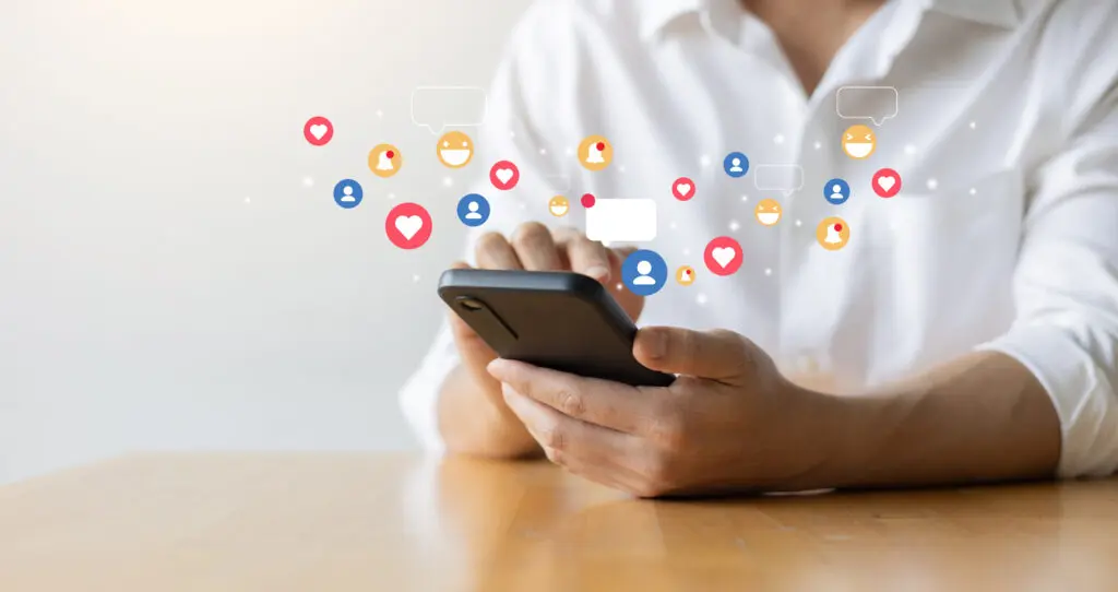 Close up of woman wearing a white blouse typing on her smartphone. There's cartoon images of 'Love', 'Like', 'Laugh', 'notification', and 'person' icons appearing to pop out of her phone.