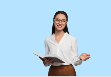 Young woman with long dark brown hair tied back, wearing large circular rimmed glasses, a white blue, and light brown trousers holding an open book with the other hand open, as if explaining something. The background is light blue.