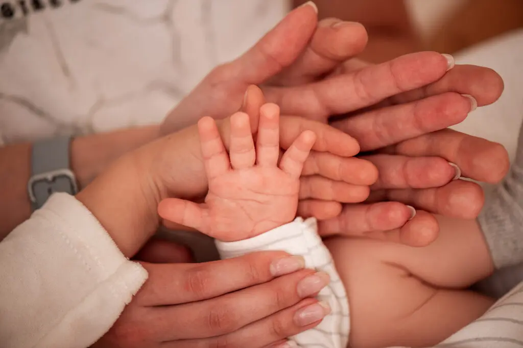 Close up of hands on top of one another. We see a father's palm, a mother's on top of it, then the palm of a young child, and a baby's palm on top.