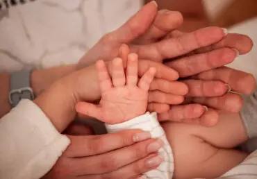 Close up of hands on top of one another. We see a father's palm, a mother's on top of it, then the palm of a young child, and a baby's palm on top.