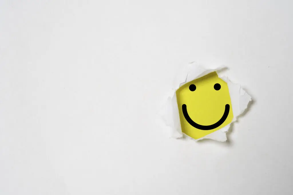 Happiness. Yellow smiley face peeking out through a hole in a piece of paper.