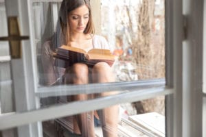 woman reading book by window