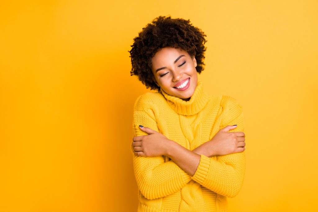 girl wearing bright yellow jumper hugging herself against a bright yellow background.
