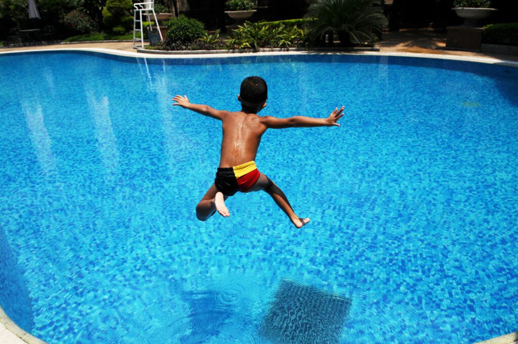 Boy leaps into swimming pool with arms outstretched