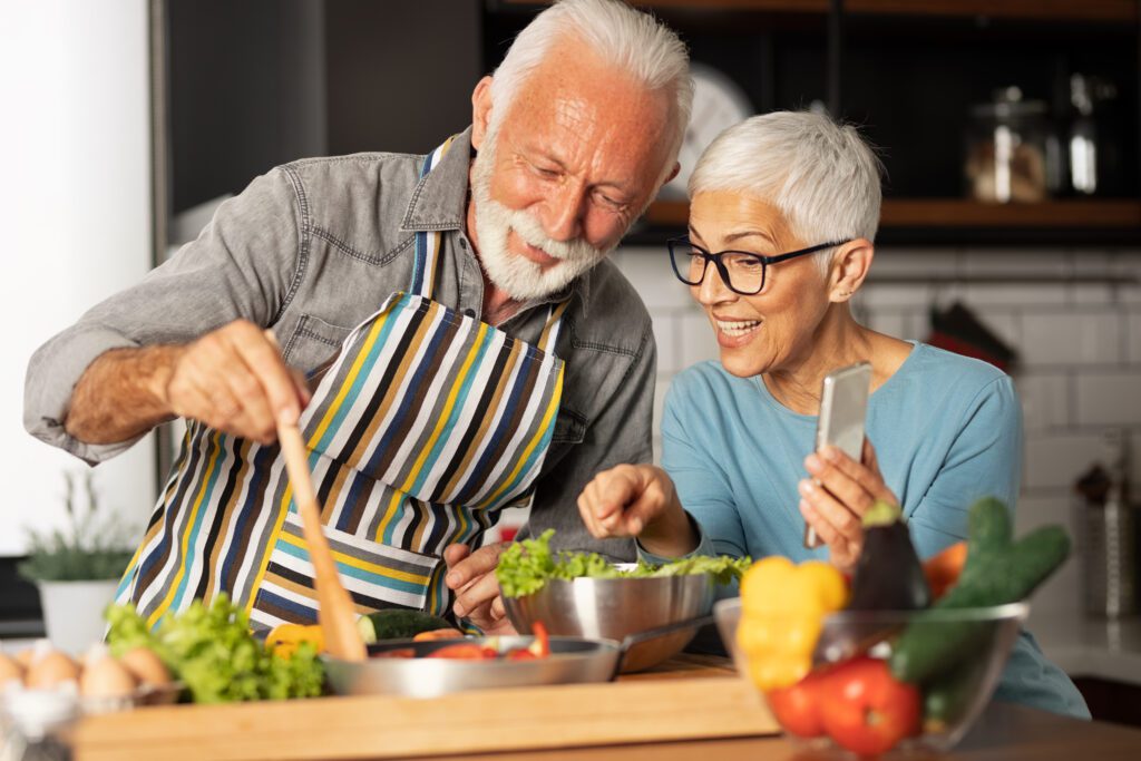 Vibrant ageing couple cooking a health meal together, smiling.