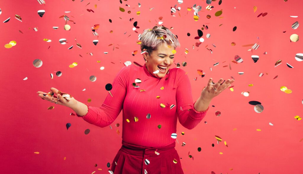 Woman celebrating. Red background. Pieces of silver paper floating.