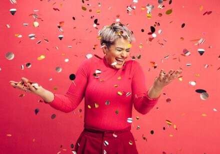 Woman celebrating. Red background. Pieces of silver paper floating.