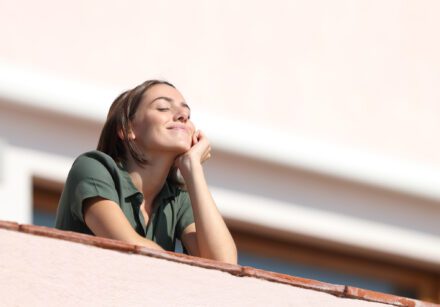 Happy woman breathing fresh air from balcony in apartment